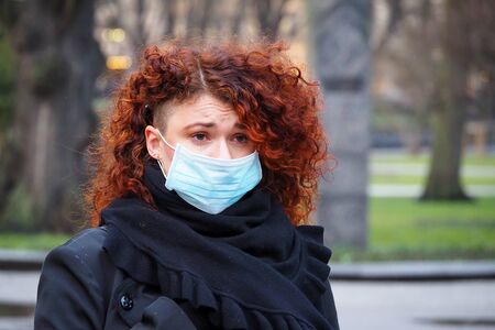Beautiful young European woman in spring clothes on the street with a medical face mask on. Closeup of a 30-year-old female in a respirator to protect against infection with coronavirus - Covid19の写真素材