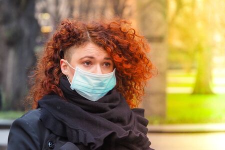 Beautiful young European woman in spring clothes on the street with a medical face mask on. Closeup of a 30-year-old female in a respirator to protect against infection with coronavirus - Covid19の写真素材
