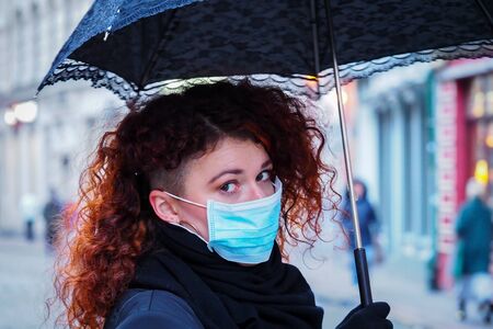 Beautiful young European woman in spring clothes on the street with a medical face mask on. Closeup of a 30-year-old female in a respirator to protect against infection with coronavirus - Covid19の写真素材