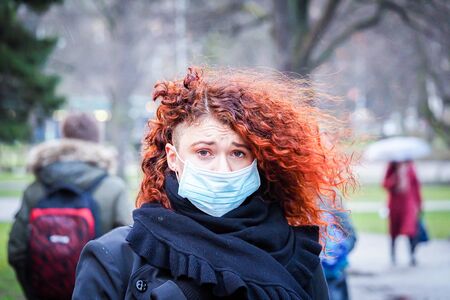 Beautiful young European woman in spring clothes on the street with a medical face mask on. Closeup of a 30-year-old female in a respirator to protect against infection with coronavirus - Covid19の写真素材