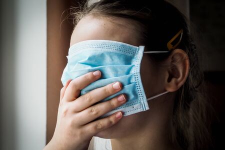 Pretty little European girl with a medical face mask on. Closeup of a 7-year-old girl in a...