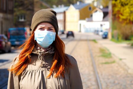 Beautiful young European woman with ginger coloured hair on the street with a medical face mask onの写真素材