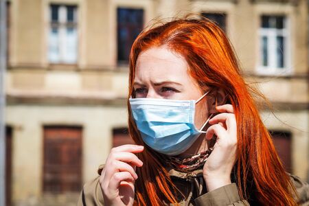 Beautiful young European woman with ginger coloured hair on the street with a medical face mask onの写真素材