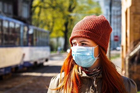 Beautiful young European woman with ginger coloured hair on the street with a medical face mask onの写真素材