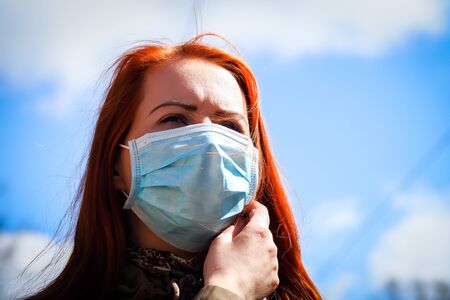 Beautiful young European woman with ginger coloured hair on the street with a medical face mask onの写真素材