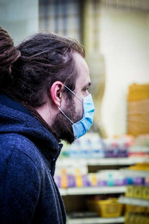 Handsome young European man with a medical face mask on looking inside the pharmacyの写真素材