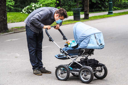 Handsome young European man on the street with a medical face mask on and baby carriage. 35-year-old male in a respirator to protect against Covid-19の写真素材