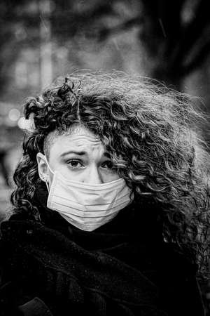 Black and white portrait of beautiful young European woman a medical face mask on to protect against...