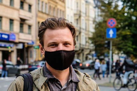 Handsome young European man in on a street with a black face mask on. Closeup of a 35-year-old male in a respirator to protect against coronavirusの写真素材