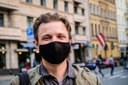 Handsome young European man in on a street with a black face mask on. Closeup of a 35-year-old male in a respirator to protect against coronavirusの写真素材