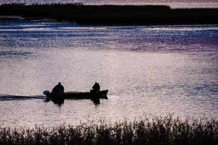 Two fishermen in the boat on a lake in the early morning sunrise, selective focus