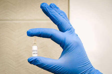 Hand in blue medical gloves holding small ampoule with label Covid-19 vaccine. Coronavirus covid 19 cure concept.の写真素材