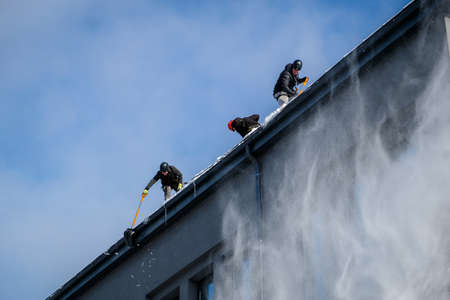 Riga, Latvia: February 12, 2021: Team of male workers clean roof of building from snow with shovels in securing belts. Selective focusのeditorial素材