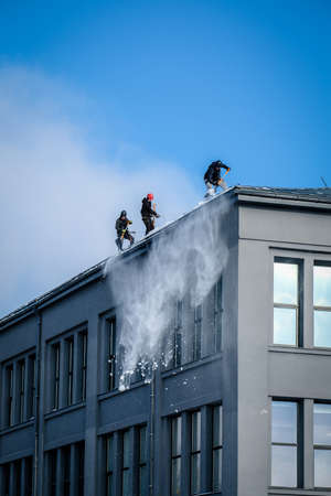 Riga, Latvia: February 12, 2021: Team of male workers clean roof of building from snow with shovels in securing belts. Selective focusのeditorial素材