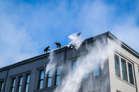 Riga, Latvia: February 12, 2021: Team of male workers clean roof of building from snow with shovels in securing belts. Selective focusのeditorial素材