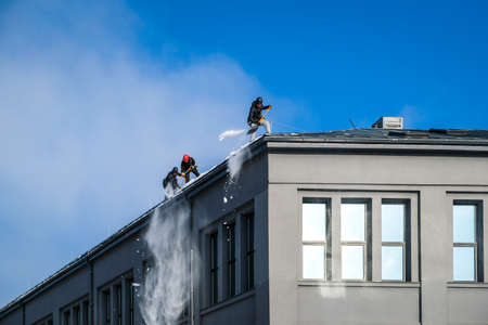 Riga, Latvia: February 12, 2021: Team of male workers clean roof of building from snow with shovels in securing belts. Selective focusのeditorial素材