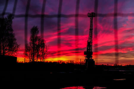 Amazing red sunrise sky with clouds over black silhouette of crane, industrial view. Selective focusの写真素材