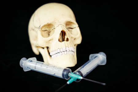 Death from the vaccine concept - human skull model and syringe.