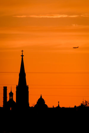 Conceptual photo of city downtown at sunset with skyline silhouette against a beautiful orange sky a airplane. Defocusedの写真素材