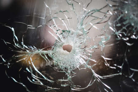 Broken window with a hole in the middle. Bullet hole in glass - real bullet hole closeup. Defocusedの写真素材