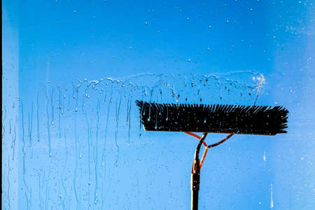 Window cleaning using telescopic water brush and wash system. Commercial window cleaning from the outside with sky in background. Defocusedの写真素材