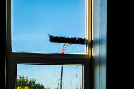 Window cleaning using telescopic water brush and wash system. Commercial window cleaning from the outside with sky in background. Defocusedの写真素材