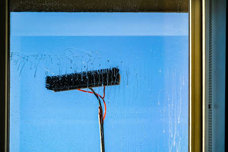 Window cleaning using telescopic water brush and wash system. Commercial window cleaning from the outside with sky in background. Defocusedの写真素材