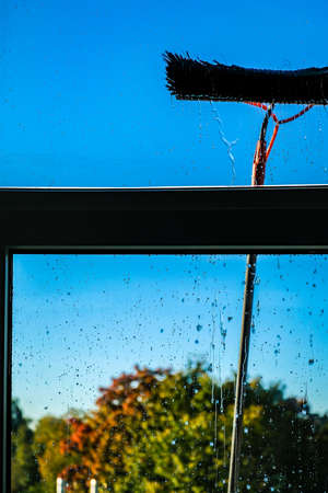 Window cleaning using telescopic water brush and wash system. Commercial window cleaning from the outside with sky in background. Defocusedの写真素材