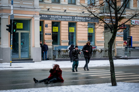 Riga, Latvia: January 17, 2022: The woman slips and falls on a slippery and icy street in winter. Slipped girl lying on the street. Selective focusのeditorial素材