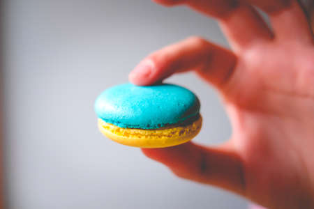The girl holds in his hand a macaroon in the colors of the Ukrainian flag. Selective focusの写真素材