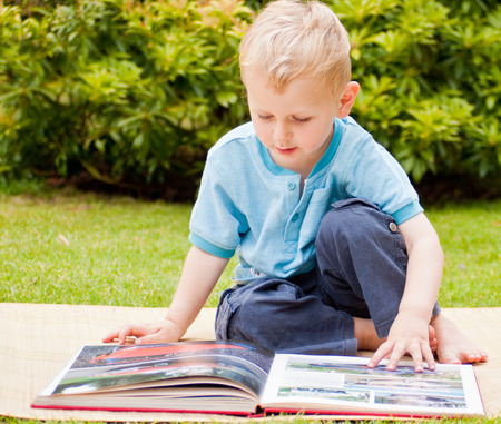 Sitting Boy Reading a Book in the Gardenの写真素材
