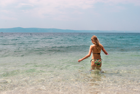 Young Caucasian female with long blond hair in bright bikini swalking into the seaの写真素材