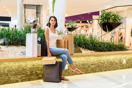 Happy Young Girl With Shopping Bags Taking A Break In Shopping Mallの写真素材