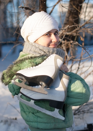 a girl holding a white skates on a background of trees in winter の写真素材