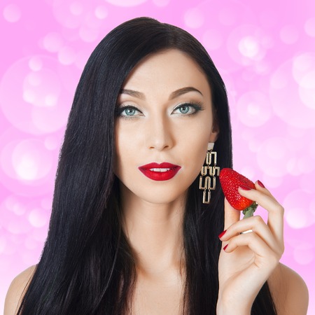 beautiful brunette with long eyelashes eating strawberriesの写真素材