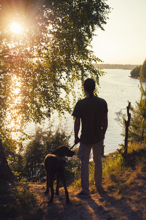 man with a dog walking in the sunset at the lakeの写真素材