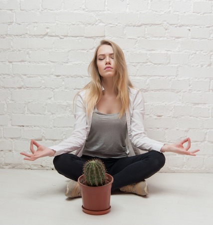 girl meditating with cactus on a background of white wallsの写真素材