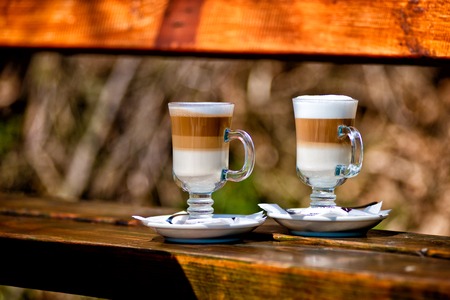 Two glasses of latte coffee beans and spoon on old wooden benchの写真素材