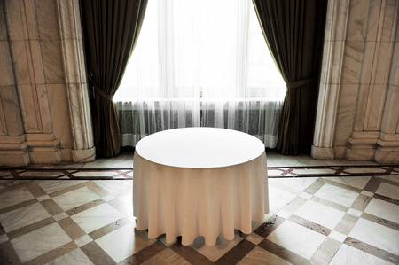 Sunlight falls on an empty round dinner table in a festive marble roomの写真素材