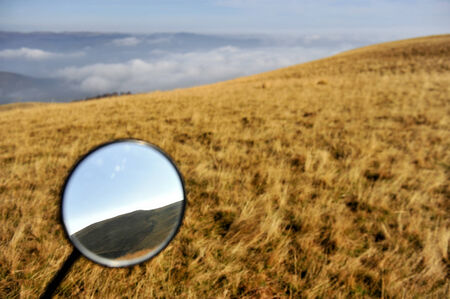 Autumn landscape with mountains reflected in a motorcycle mirrorの写真素材