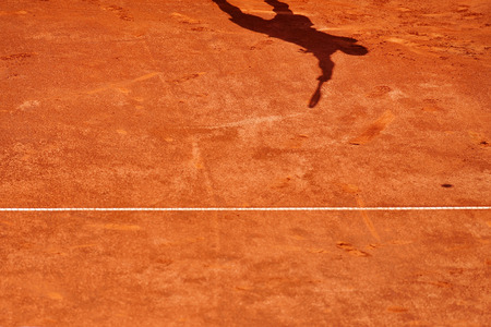Shadow of a tennis player serving on a clay courtの写真素材