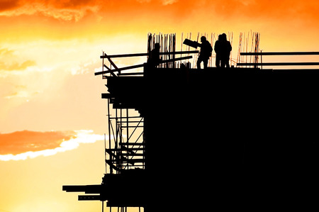 Construction workers silhouettes on a construction site at sunset