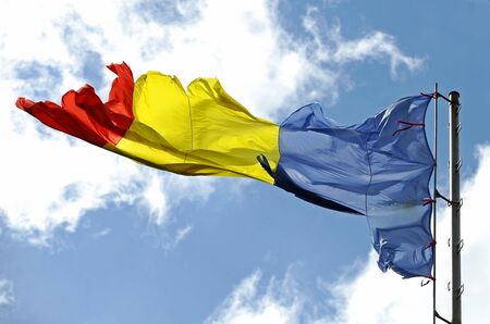 Romanian flag ripped of by the wind with blue sky on backgroundの写真素材