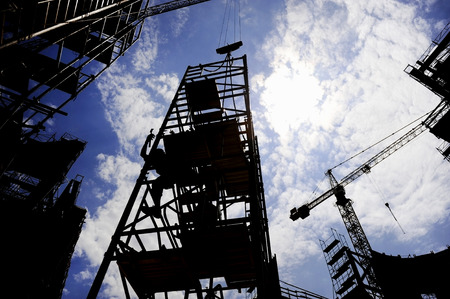 Industrial shot with construction worker silhouetted against blue sky working on a scaffoldの写真素材