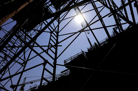 Industrial shot with construction worker silhouetted against blue sky working on a scaffoldの写真素材