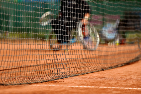 Unfocused wheelchair tennis player is seen behind a tennis net on a clay courtの写真素材