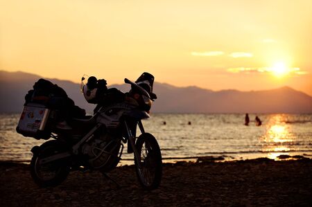 SHKODRA, ALBANIA - AUGUST 21: Adventure motorcycle loaded with luggage on the shore of Shkodra Lake at sunset on August 21, 2015 in Albania.のeditorial素材