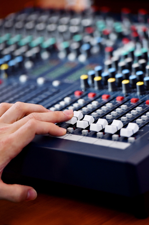 Detail with a hand adjusting sound levels on a professional audio mixer