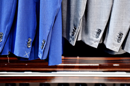 Elegant blue and gray suits on hangers are seen in a suit storeの写真素材