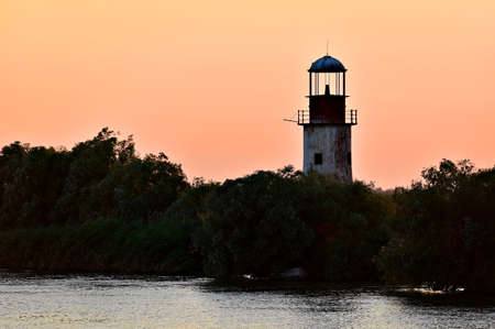Abandoned old and weathered lighthouse at sunet on a riverの写真素材
